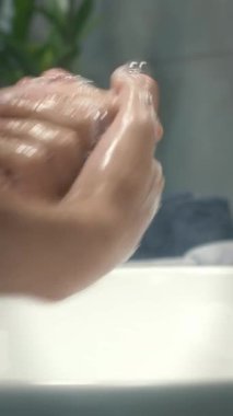 Hand washing to prevent infection. Woman washes hands with soap in sink at modern bathroom. Female is washing and lathering hands with foam. Vertical video