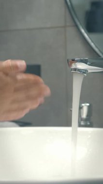 Female opening sink tap, starting to wash hands with soap and wiping them with towel, close up of sink and hands. Vertical video