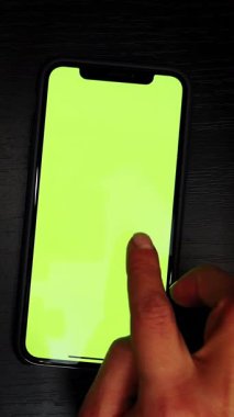 Hand using smartphone with green screen chroma key, scrolling news, tapping on photos. Female watching photos on mobile phone with green screen. Vertical video