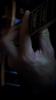 Close up of male hand playing on guitar strings, learning new chords. Professional musician plays on electric guitar in dark studio. Vertical video