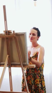 Artist paints on canvas and smears a brush. Canvas stands on the easel. Woman drawing at easel. Female painting at art studio. Vertical video