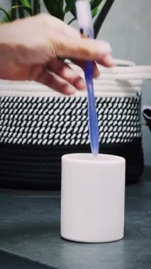 Erkek el, diş fırçalarını banyodaki beyaz plastik bardağa koyup, kapatıyor. El, iki plastik renkli diş fırçasını deney şişesine koyuyor. Dikey video