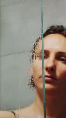 Ev hanımı banyoda cam duş kabini kapılarını paçavrayla yıkıyor. Temizlik ürünleri, cam yüzeyler için temizlik malzemesi. Kadın küveti siliyor. Dikey video