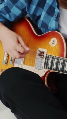 Elektro gitarlı bir kadın şarkılar çalıyor, ellerini ve tellerini kapatıyor. Gitarda çalan eller telleri ve akorları çekiyor. Müzik konsepti. Dikey video