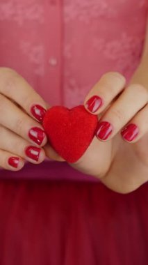 Küçük kırmızı kalp, kadınların ellerinde, yaklaşın. Kadının elinde Sevgililer Günü için kırmızı kalp hediyesi var. Kadın, kırmızı kalbin kameraya doğru ilerlediğini gösteriyor. Dikey video