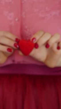 Küçük kırmızı kalbi elinde tutan bir kadın. Sevgililer Günü konsepti. Eller kırmızı kalp hediyesini tutuyor. Kadın Sevgililer Günü için küçük kırmızı bir kalp gösteriyor. Dikey video