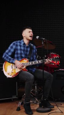 Erkek sanatçı duygusal olarak aşk şarkısı söylüyor ve gitar çalıyor. Elektro gitarda çalan ve mikrofona şarkı söyleyen bir müzisyen. Profesyonel kayıt stüdyosu. Dikey video