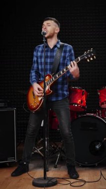 Erkek mikrofona şarkı söylüyor ve ses stüdyosunda elektro gitarla çalıyor. Erkek şarkıcı, söz aşkı şarkısı söylüyor ve kayıt stüdyosunda gitar çalıyor. Dikey video