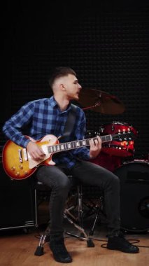 Profesyonel gitarist elektro gitarist, modern prova stüdyosunda solo gitar çalıyor. Müzisyen karanlık odada yeni akorlar ve şarkılar öğreniyor. Dikey video