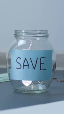 Bozuk paralar kelime tasarrufu ile cam kavanoza düşer. Gelecek için yatırım. Avro para ve sikkeler arasında masada yazılı olan şeffaf bir kavanoz. Dikey video