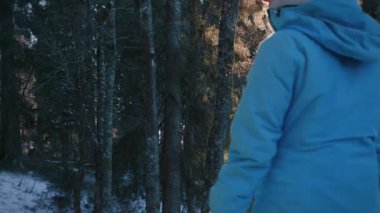 Young hiker walking along footpath in winter forest covered with snow. Female explorer hiking in nature park with pine trees, adventure outdoor. Travel and active lifestyle concept