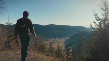Male traveller with backpack and map in hands standing on edge of mountain summit and looking at picturesque mountain ranges, searching for direction. Travel and tourism concept