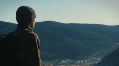 Man in sportswear with backpack on mountain top looking to surrounding peaks, exploring nature. Male traveller standing on edge of mountain and enjoying picturesque landscape