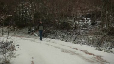 Man in sportswear with backpack walking along snowy footpath in forest. Male explorer hiking in winter forest, enjoying picturesque nature landscape. Travel and tourism concept