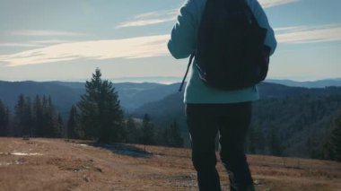 Female traveler with backpack hiking in mountains, enjoying nature. Woman explorer walking on mountain trail on hike. Freedom adventure and explore nature. Travel and tourism concept