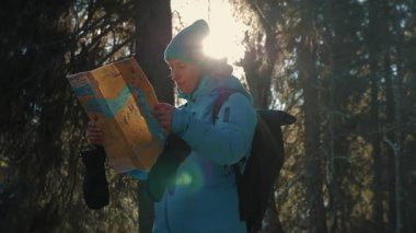 Mavi spor ceketli ve şapkalı bir kadın elinde haritayla yön arıyor, kışın doğayı keşfediyor. Seyahat ve turizm kavramı
