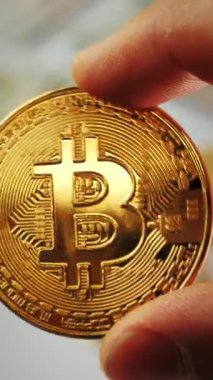 Close up of hand holds gold bitcoin against money and coins background. Mining and trading. Cryptocurrency. Vertical video