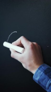 Man writing word closed with white chalk on blackboard. 