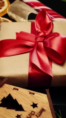 Wrapped with red ribbon gift box rotating against christmas decorations, close up. Christmas gift wrapped in craftool paper with red tape. Vertical video