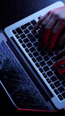 Top view of opened laptop with hands typing on keyboard in dark office. Hacker is coding and programming virus security system on screen laptop in dark room. Male is typing code. Vertical video