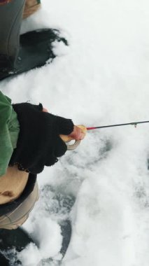 Close up of fisherman hands and fishing rod. Fisherman is catching fish in ice hole. Man is fishing on frozen river. Winter fishing concept. Vertical video
