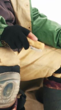 Man in winter clothes with fishing rod is catching fish in ice hole. Fisherman is fishing on frozen lake. Vertical video