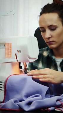 Woman in casual clothes is sewing fabric on sewing machine. Portrait of professional female seamstress in tailor's studio. Vertical video
