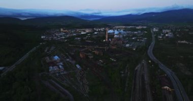 Üretim Fabrikaları Gün doğumuna kadar bacalar Ilık, hafif, bulutlu dağlar Uzakta, havadan yüksek irtifada, sabit bir drone.
