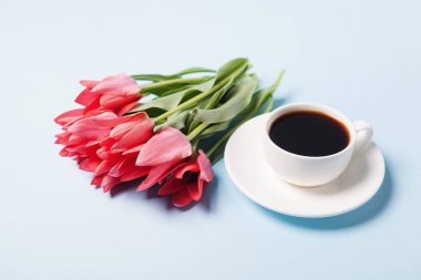 Bir fincan çay tabağında kahve ve mavi arka planda bir buket lale.