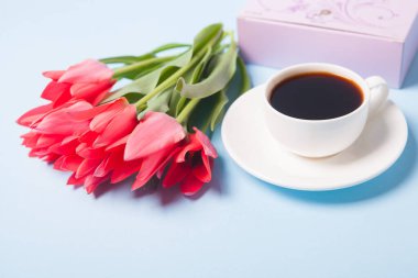 Bir fincan çay tabağında kahve ve mavi arka planda bir buket lale.