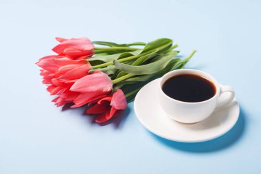 Bir fincan çay tabağında kahve ve mavi arka planda bir buket lale.