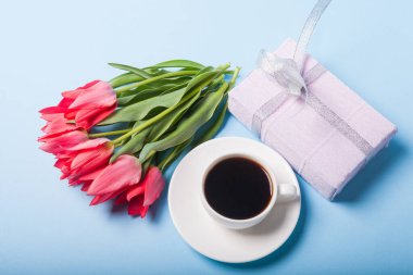 Bir fincan çay tabağında kahve ve mavi arka planda bir buket lale.