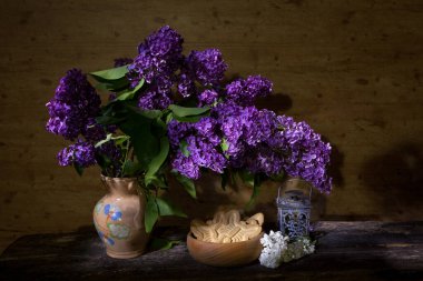 Hasır sepette kurabiyeler, çay tabağında kahve ve açık ahşap bir yüzey üzerinde bir buket lale.