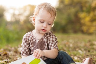 Sonbahar parkında güneşli bir günde kareli bir battaniyede oturan küçük kız..