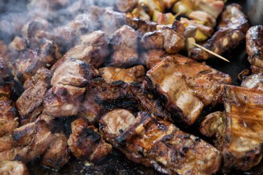 Dışarıdaki barbeküde ızgara yapılan bir sürü et parçasının yakın çekimi. Barbeküde bir sürü et ve farklı bir dokuda duman var. Sokak yemekleri festivali.