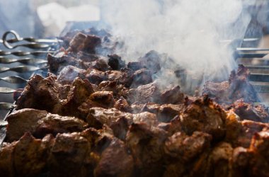Dışarıdaki barbeküde ızgara yapılan bir sürü et parçasının yakın çekimi. Barbeküde bir sürü et ve farklı bir dokuda duman var. Sokak yemekleri festivali.