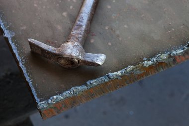 Yaşlı bir kaynakçının çekici kalın bir metal parçasına oturur..