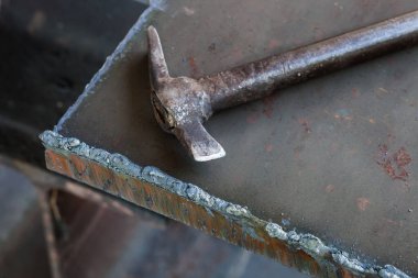 Yaşlı bir kaynakçının çekici kalın bir metal parçasına oturur..