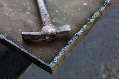 Yaşlı bir kaynakçının çekici kalın bir metal parçasına oturur..