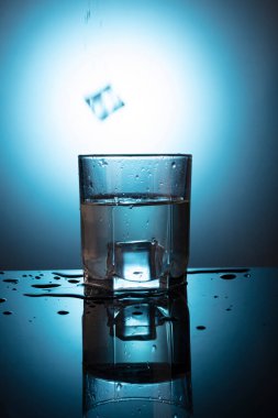 Mavi zemin üzerinde su olan bir bardak..