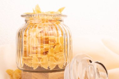 Çeşitli çiğ makarnaların yakın çekimi. Beyaz masada kompozisyon. Kavanozda çiğ makarna. Seçici odak.