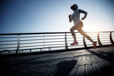 Fitness kadın koşucusu deniz kenarındaki köprüde koşuyor.