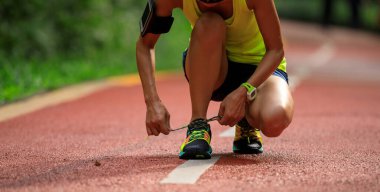 Güneşli tropikal park yolunda ayakkabı bağı bağlayan kadın koşucu
