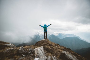 Kadın yürüyüşçü, dağın tepesindeki uçurumun keyfini çıkar. Tibet 'teki kar kaplı dağlara bak.