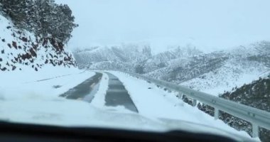 Karlı dağlardaki yolda giden arabanın hava görüntüsü.