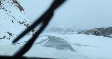 Karlı dağlardaki yolda giden arabanın hava görüntüsü.