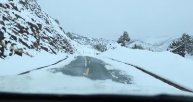 Karlı dağlardaki yolda giden arabanın hava görüntüsü.