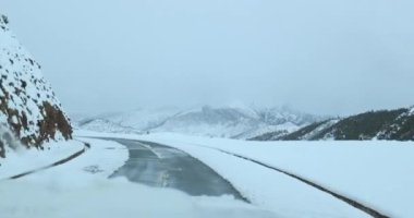 Karlı dağlardaki yolda giden arabanın hava görüntüsü.