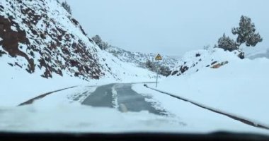 Karlı dağlardaki yolda giden arabanın hava görüntüsü.
