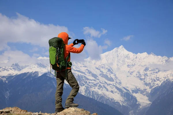 スマートフォンで標高の高い山の写真を撮る女性バックパッカー — ストック写真